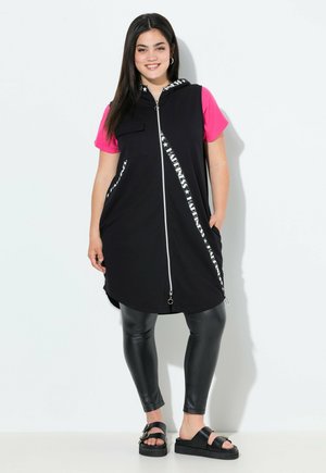 Black sleeveless dress with a pink shirt, featuring a zipper front, side pockets, and "HAPPINESS" printed in white across the front. Paired with black leather leggings and sandals.