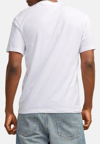 White cotton t-shirt with a relaxed fit, short sleeves, and a curved neck. Worn with light blue denim jeans featuring back pockets.