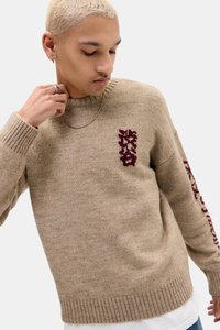 Beige ullgenser med ribbestrikkede mansjetter og kant, med burgunderrødt grafisk motiv på brystet og mønsterdesign langs ermet.