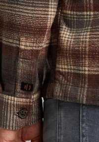 Bruin en beige geruite flanellen overhemd met een knoopmanchet en label. Een zachte, textuurachtige stof en een recht gesneden ontwerp zijn zichtbaar.