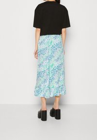 T-shirt noir court associé à une jupe bleu clair ornée d'un imprimé floral vert et bleu, avec un ourlet texturé et des chaussures compensées noires.