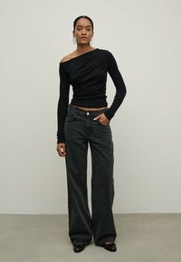 Juodas ilgomis rankovėmis viršus su nuolaida pečiams, derinamas su laisvai krintančiomis tamsiomis džinsomis. Išvaizdą užbaigia plokščios juodos batai.