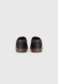 Sorte sneakers med brune gummisåler, med en glat læderoverdel, rund tådesign og subtil branding på hælen.
