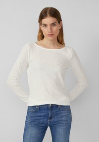 White long-sleeve shirt in a soft, lightweight fabric with a boat neckline, paired with blue denim jeans. Simple, clean design.