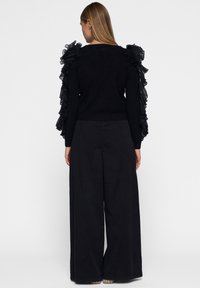 Zwarte trui met getextureerde, gerimpelde tule mouwen. Gecombineerd met zwarte wijde broek. Glad materiaal, minimalistisch ontwerp en effen kleur.