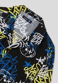 Camicia a maniche corte con un tessuto nero coperto da pattern in stile graffiti colorati in blu, giallo e bianco, con colletto a pieghe.