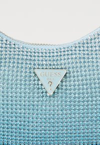 Bolso de mano azul claro cubierto de pequeños y brillantes rhinestones. Presenta una placa triangular de plata con el nombre de la marca "Guess U.S.A."