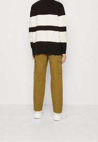 Suéter a rayas en blanco y negro con un ajuste relajado, combinado con pantalones cargo caqui que presentan bolsillos laterales y piernas entalladas. Zapatillas blancas visibles.