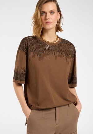 Camiseta marrón de manga corta, con un patrón decorativo de lentejuelas en el hombro y el escote. Tela suave, corte relajado.