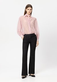 Light pink button-up blouse with long sleeves and a tie detail at the collar, paired with black flared trousers. Smooth fabric, subtle texture.