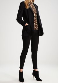 Musta räätälöity bleiseri, jossa on taskut, leopardikuosisen paidan päällä, yhdistettynä mustiin slim fit -farkkuihin ja mustiin korkokenkiin nilkkamallissa. Sujuva pinta.