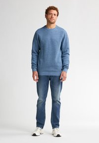 Pulover tricotat texturat, de culoare albastră, cu guler rotund, asociat cu blugi de culoare albastră deschisă și adidași albi. Are o croială lejeră și manșete cu rimă.