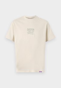 Lys beige bomulls t-skjorte med korte ermer og rund hals. Den har et trykt grafisk motiv i grønt på forsiden og en lilla etikett på siden.