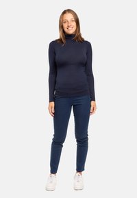 Maglione a collo alto navy a maniche lunghe, design aderente, abbinato a jeans slim scuri e sneaker bianche. Tessuto semplice e liscio, senza motivi visibili.