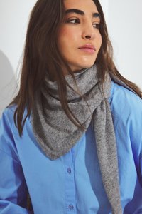 Harmaa villahuivi, kolmiomainen muoto, ripustettuna kaulan ympärille, yhdessä sinisen napitettavan paidan kanssa. Kangas näyttää pehmeältä ja teksturoidulta.