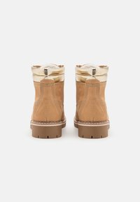 Stivaletti alla caviglia in suede beige con un bordo dorato lucido, fodera in pile bianco e suola in gomma testurizzata. Dettagli cuciti lungo le cuciture.