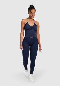 Marinblå sport-bh med halterneck-design och rynkning, tillsammans med marinblå leggings. Båda är tillverkade av elastiskt material med en slät yta.