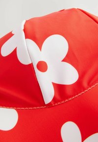 Cappello da sole rosso realizzato in tessuto liscio, caratterizzato da grandi motivi floreali bianchi con un punto centrale, cuciture a punto e un design a corona arrotondata.