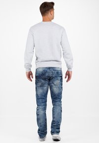 Un sweat-shirt gris à manches longues. Un jean en denim bleu avec un délavage clair, une texture usée et deux poches arrière. Des baskets blanches.