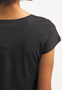 Černá košile s krátkým rukávem, zaobleným výstřihem, hladkým povrchem a přiléhavým střihem, zobrazena ze zadní strany, s viditelnými rameny a paží.