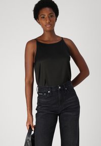Top negro sin mangas hecho de un tejido suave, combinado con jeans oscuros de tiro alto. El conjunto presenta un diseño minimalista.