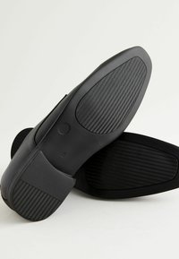 Zwarte schoenen met een gladleren bovenwerk en gestructureerde rubberen zolen. De zool heeft een visgraatpatroon voor grip.