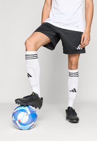 Μαύρο αθλητικό σορτς, λευκές αθλητικές κάλτσες με μαύρες ρίγες και μαύρα παπούτσια ποδοσφαίρου, με μια μπλε και λευκή ποδοσφαιρική μπάλα κάτω από το πόδι.