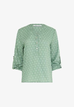 Hellgrüne Langarmbluse mit weißem rechteckigem Punktmuster, drei Knöpfen vorne und hochgekrempelten Ärmeln, die mit Laschen befestigt sind.