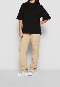 Černé oversize tričko, béžové cargo kalhoty s bočními kapsami a bílé sportovní boty. Neformální, uvolněný střih s krátkými rukávy a minimálním designem.