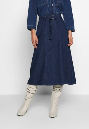 Denimnederdel i mørkeblå, A-line design med en belagt talje, der har en glat tekstur og synlige sømdetaljer. Sammen med cremede knæhøje støvler.