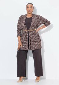 Cardigan largo con estampado animal y mangas 3/4, ceñido en la cintura con un cinturón. Debajo, una camiseta de manga larga oscura combinada con pantalones oscuros de pierna ancha.