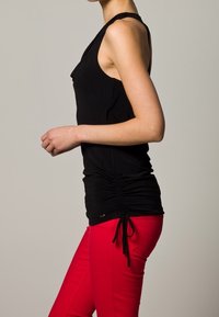 Zwarte mouwloze top met geplooide zijkanten, gecombineerd met felrode slim-fit broek van gladde stof.