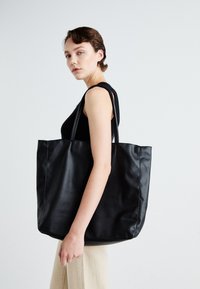 Velika črna torba iz teksturirane usnjene, z dvema dolgima trakovoma in prostornim dizajnom. Brez vidnih kovinskih delov ali vzorcev.