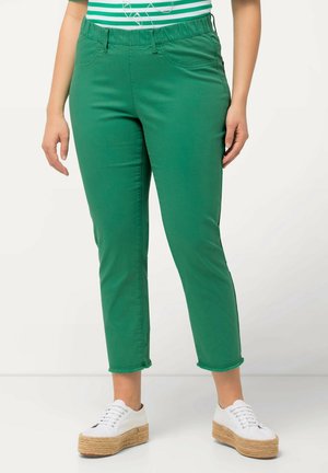 Zelené kalhoty s elastickým pasem a slim fit, vykrojená délka a třepené lemy. Bílé platformové tenisky dokončují vzhled.