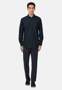 Camicia a bottoni in denim scuro con colletto a punta, maniche lunghe e una leggera texture, abbinata a pantaloni scuri sartoriali e sneakers blu navy.