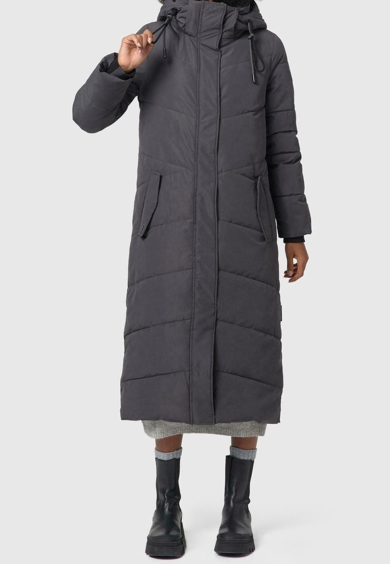 Lang, mørkegrå puffjakke med høj krave, lynlås foran, skrå syninger, to lommer og en løs pasform, båret over en lys sweater.
