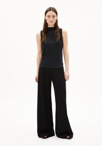 Top nero senza maniche con collo alto abbinato a pantaloni neri a gamba larga. Texture liscia, design minimalista, senza motivi o accenti visibili.