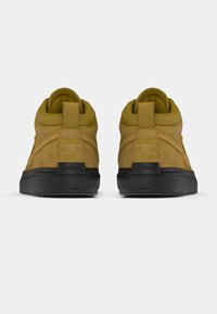 Baskets montantes en daim beige avec semelles en caoutchouc noir. Elles comportent un col rembourré, une semelle extérieure en caoutchouc et des détails de surpiqûres contrastantes.