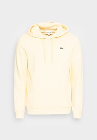 Ljusgul Lacoste-hoodie med framfickor, dragsko i huvan och liten grön krokodil-logga på bröstet.