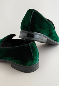 Green velvet slip-on shoes with a low black rubber sole. Features a smooth texture and rounded back design.