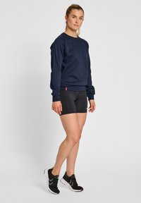 Sudadera azul marino de tejido texturizado, cuello redondo y puños acanalados, combinada con shorts ajustados negros y zapatillas deportivas negras.
