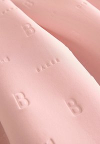 Světle růžová textilie s hladkým povrchem a reliéfními písmeny "B" a "BALI", zdůrazňující decentní branding a minimalistický design.