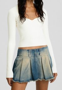 Haut blanc à manches longues côtelé avec un décolleté en cœur, associé à une mini-jupe plissée en denim bleu clair, avec un ourlet effiloché.