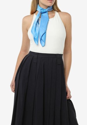 Top blanco de cuello halter combinado con una falda negra plisada. Una bufanda de seda azul clara atada al cuello añade un acento contrastante.