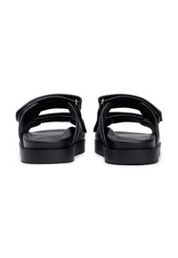 Μαύρα σανδάλια από απαλό, λείο υλικό, με τρεις ρυθμιζόμενους ιμάντες και χοντρή σόλα. Μινιμαλιστικός σχεδιασμός χωρίς εμφανή μεταλλικά μέρη.