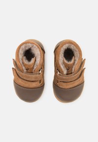 Stivaletti per bambino in suede e pelle marrone con due cinturini regolabili in velcro, fodera in feltro morbido e suola in gomma. Forma della punta arrotondata.