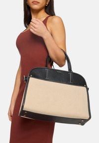 Structured handbag featuring a black leather top and beige canvas body with stitching accents. Dual top handles for carrying.