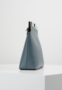 Läderklutchväska i dämpad blå färg, triangulär form, med silverlås och svarta accenter, slät textur och minimalistisk design.