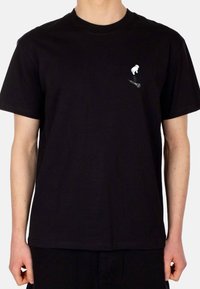 Zwarte katoenen t-shirt met een kleine witte afbeelding van een vogel en een microfoon op de linkerborst. Klassieke ronde hals en korte mouwen.