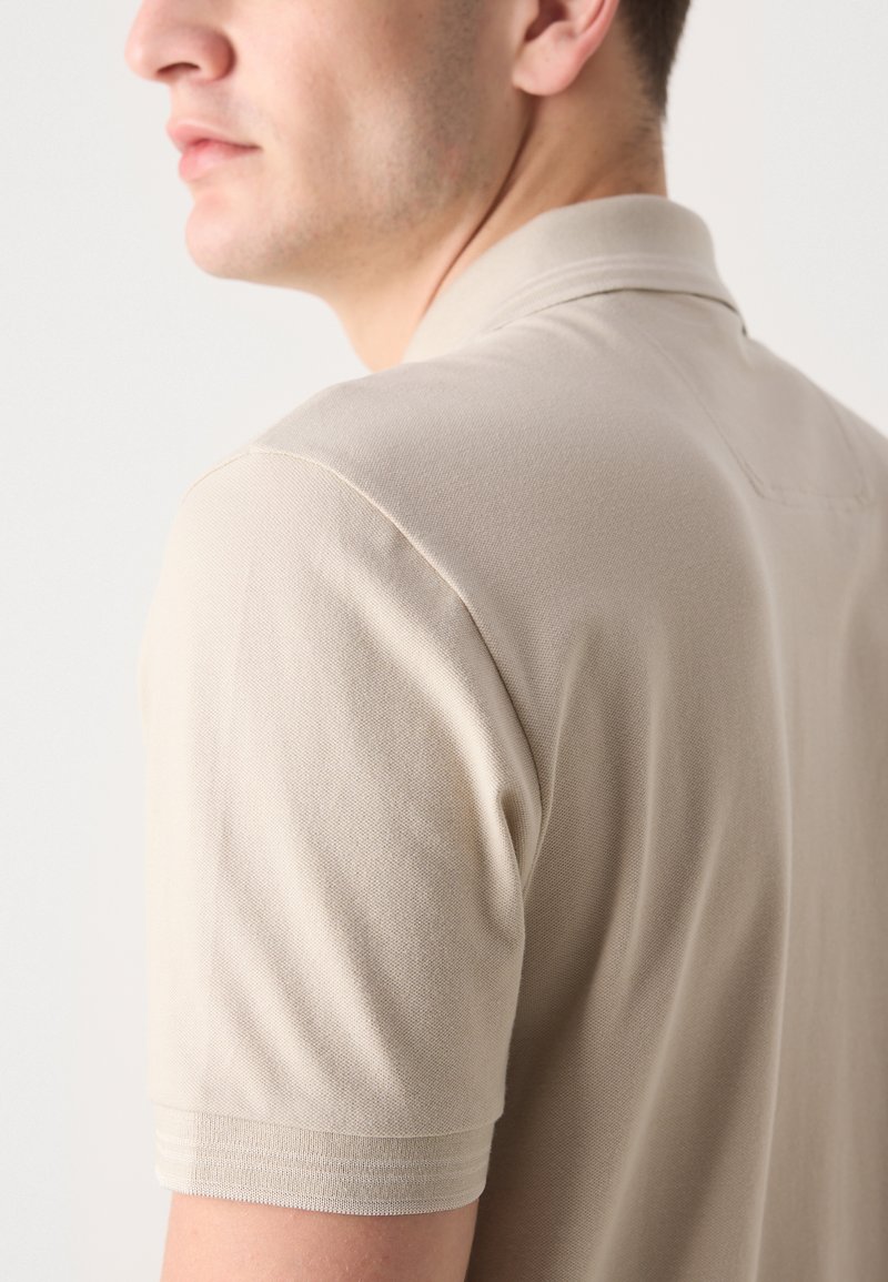 Polo shirt beige à manches courtes, en tissu texturé, avec un col classique et un design simple et épuré.